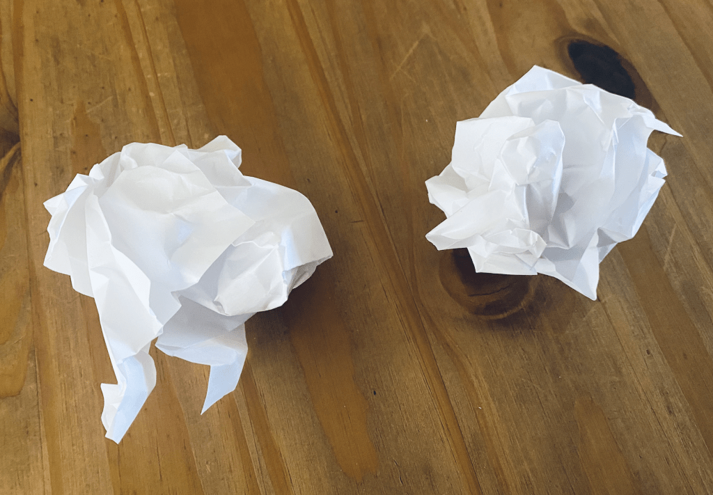 On a wooden table, two scrunched up pieces of paper in preparation for the treats and a paper challenge. 