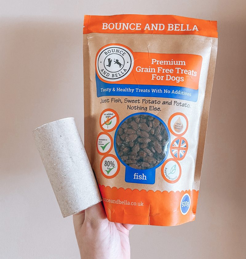 Treat Roll Game Feature Photo: A Hand holding packet of grain-free training treats with a toilet roll holder.